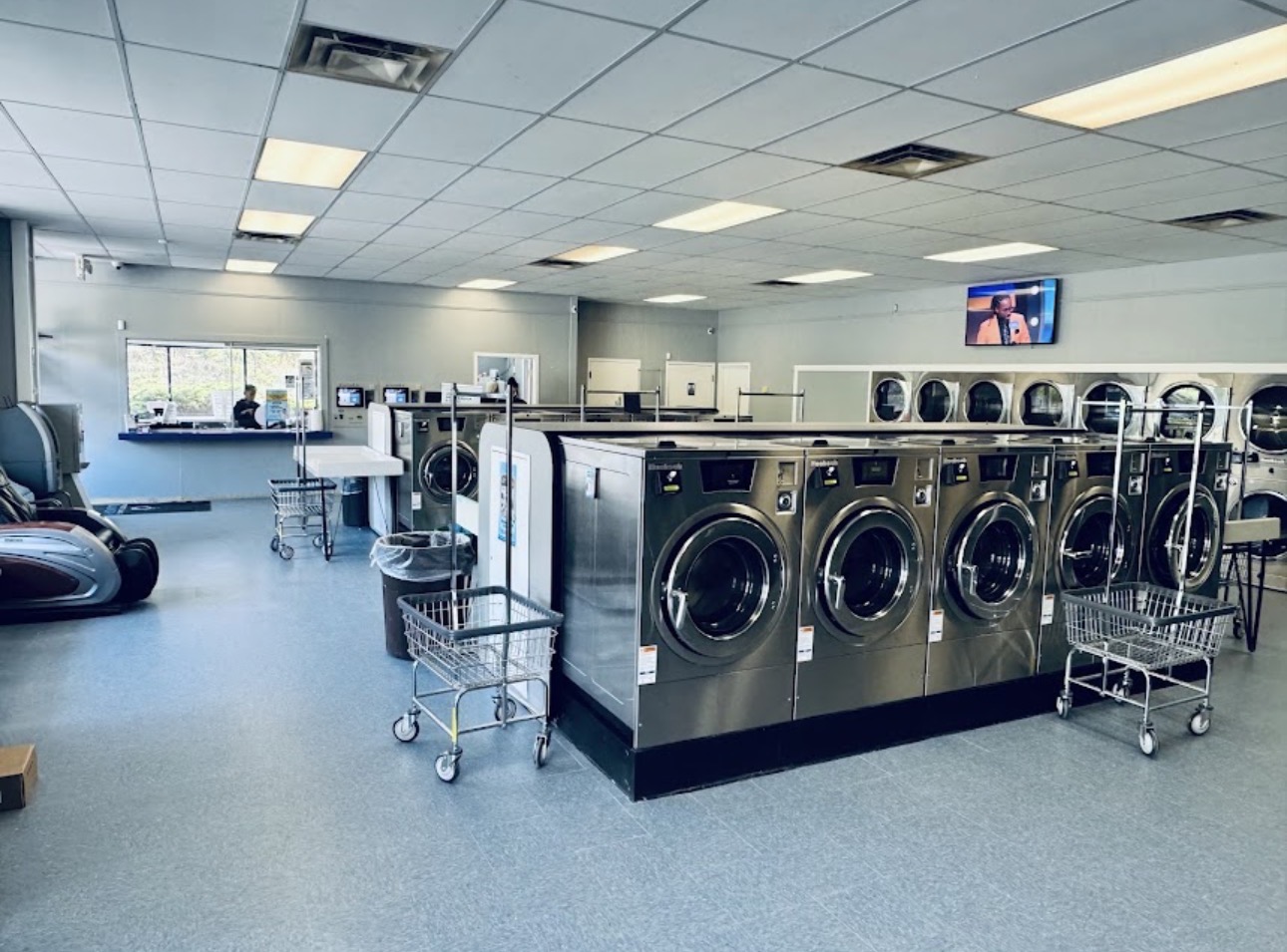 Interior of Pocket Change Laundry on New Leicester Highway in Asheville, North Carolina showing stainless steel washers, laundry carts, massage chairs and a flat-screen television