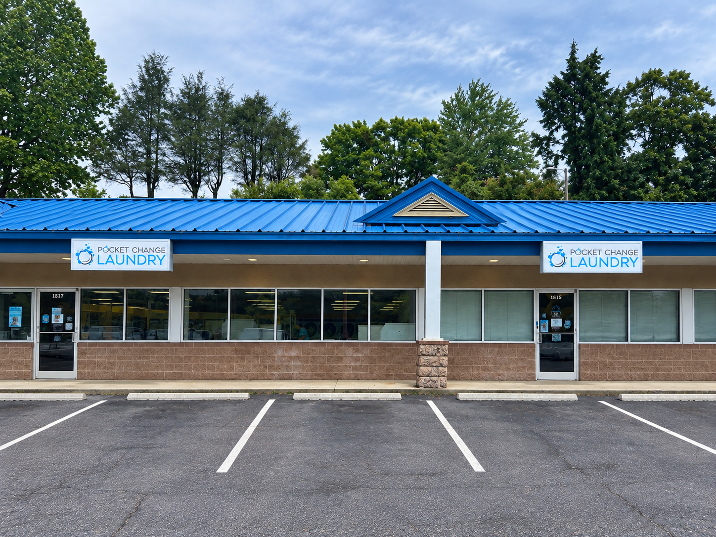 Pocket Change Laundry storefront on Smokey Park Highway in Candler, North Carolina showing two branded entrances, a bright blue roof, large windows, and parking in front