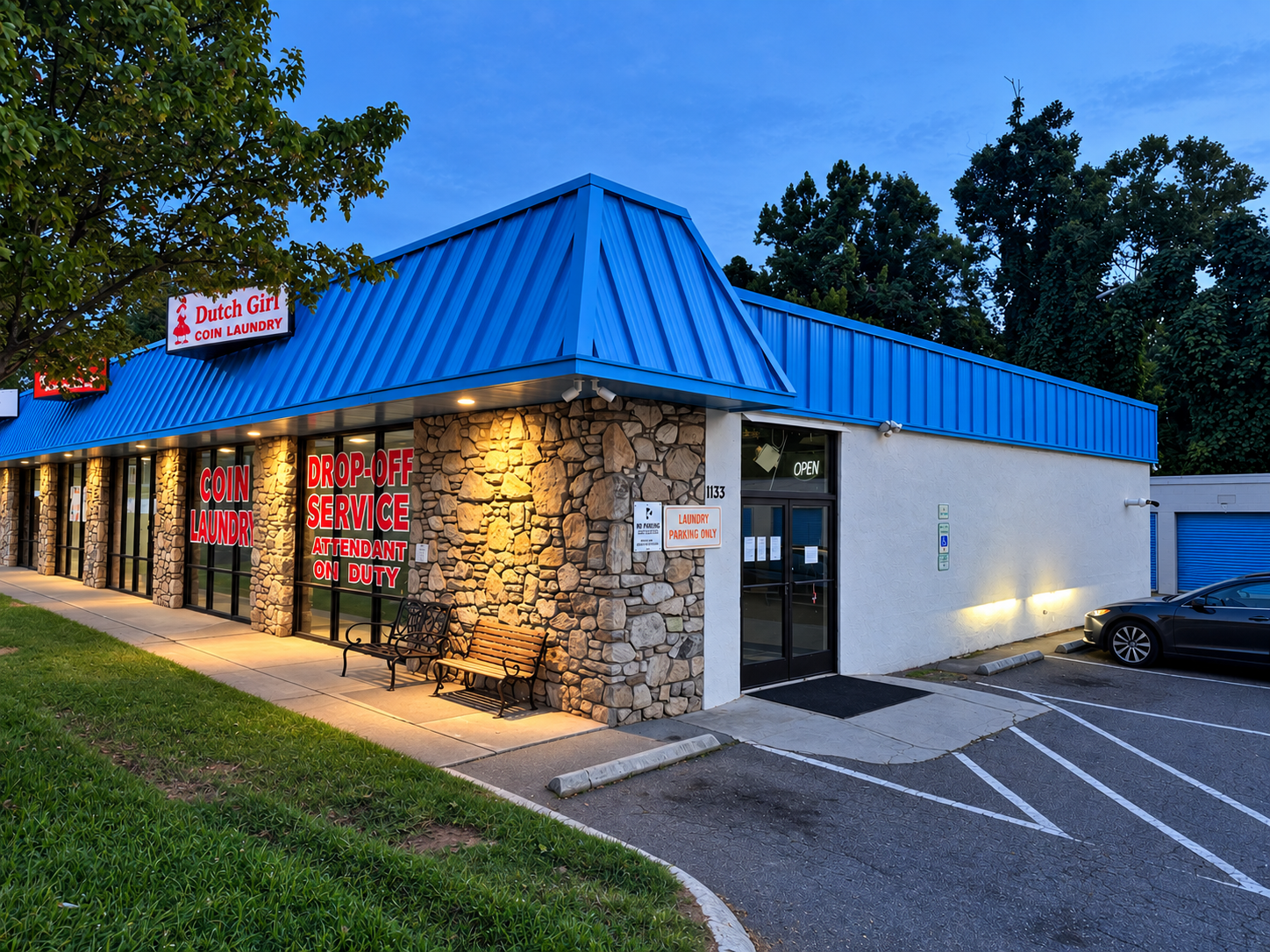 Dutch Girl on Sweeten Creek storefront at 1133 Sweeten Creek Road in Asheville, North Carolina, with a blue roof, stone facade, drop-off service signage and parking at dusk